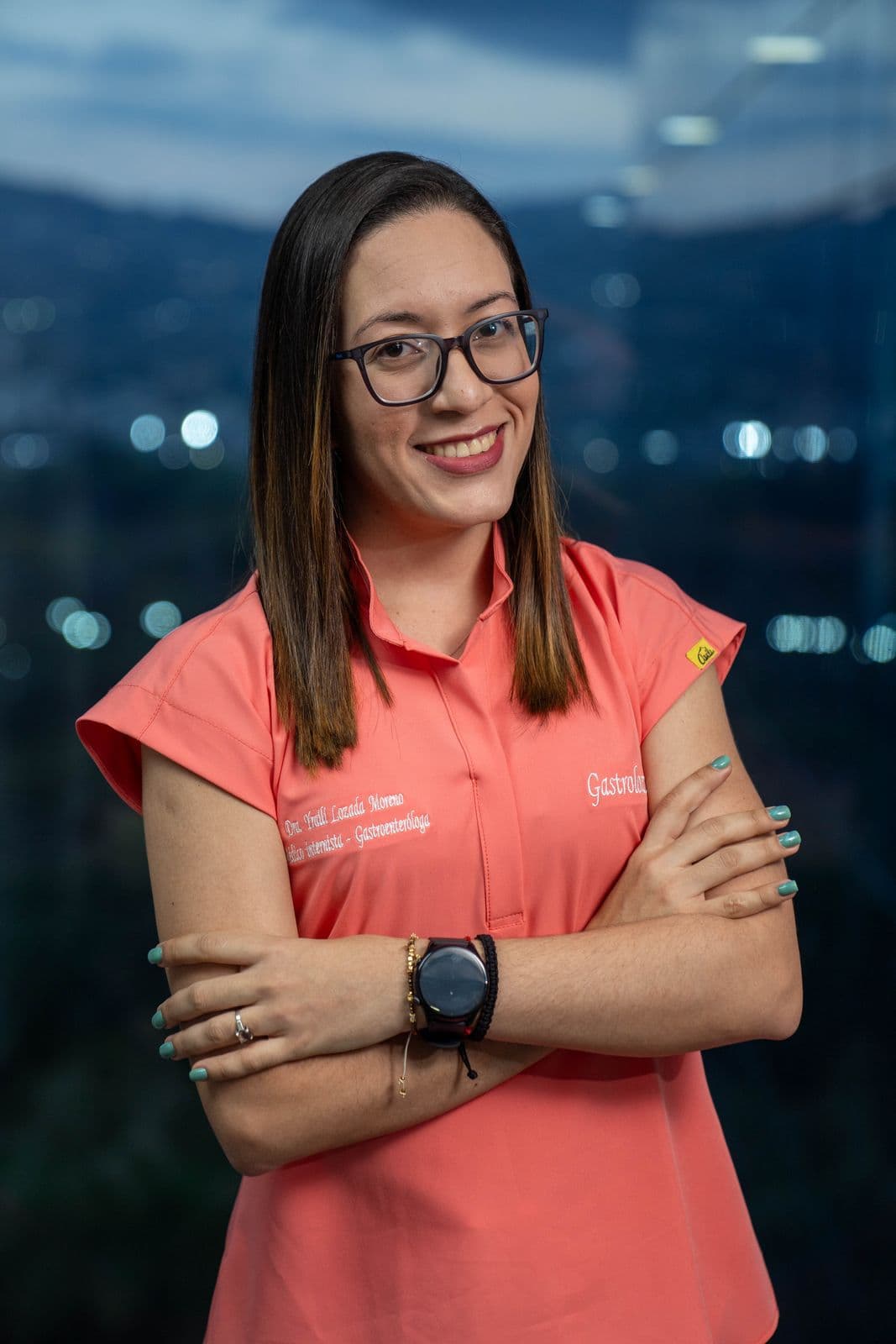 Retrato de la Dra. Yraili Lozada con blusa coral y los brazos cruzados, con la ciudad de noche al fondo